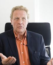 Ein Mann spricht in einem professionellen Umfeld vor der Kamera. Seine Gestik und Mimik vermitteln Offenheit, Kompetenz und Vertrauen.