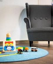 Kinderecke mit einem türkisen Teppich und Spielzeug. Dahinter ein grauer Kindersessel.