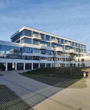 Weißes Gebäude mit mehreren Fenstern und Balkonen. Davor Grünflächen und Pflastersteine