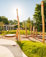 Außengelände des Fröbel-Kindergartens Essener Straße mit Naturspielbereich aus Holzstämmen, Balancierelementen und begrünten Flächen.
Fröbel-Kindergarten Essener Straße, Hamburg, © Fröbel, Foto: Martin Arnold. Alle Rechte vorbehalten.
