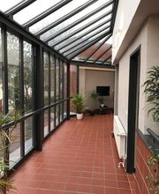 Flur mit roten Fliesen und Glasdach. Hinten stehen Pflanzen und ein TV hängt an der Wand.