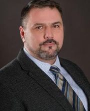 Portrait vom Bildungsreferent Manuel Normann. Ein Mann mit dunklen Haaren und Bart, der einen Anzug und Krawatte trägt.