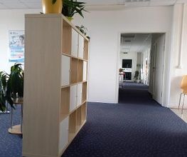 Aufenthaltsbereich mit links hell braunem Regal und Teppichboden