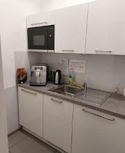 Eine weiße Küche mit Kaffeemaschine, Wasserkocher, Waschbecken und Mikrowelle.