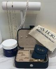 Na Hoku gold and pearl jewelry propped on stand and in jewelry box, showing pouches and cleaning supplies, all set up on a white, marbled vanity.