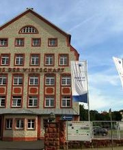 Ein Bild der Außenansicht des Kooperationsstandortes in Grimma. Das Haus hat eine beige Fassade und rote Ränder. Es gibt einen roten Schriftzug „Haus der Wirtschaft“.