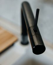 Die Nahaufnahme zeigt eine hochwertige, mattschwarze Design-Küchenarmatur von Quooker mit minimalistischer Formensprache. Der Fokus liegt auf der eleganten Linienführung und der präzisen Verarbeitung der Armatur, während der Hintergrund durch eine geringe Tiefenschärfe dezent verschwimmt. Die moderne Armatur fügt sich harmonisch in das exklusive Küchendesign ein und unterstreicht den zeitlosen Charakter hochwertiger LEICHT Küchen.