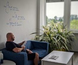Ein Mann sitzt auf einem blauen Sofa und liest etwas.