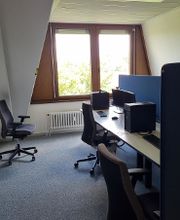 Ein Schulungsraum mit mehreren Arbeitsbereichen, die durch blaue Trennwände voneinander getrennt sind. Jeder Arbeitsplatz besteht aus 2 PC-Bildschirmen, Tastatur und Maus sowie Headset und blauen Trennwänden.