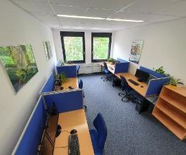 Schulungsraum mit mehreren Arbeitsbereichen, die durch blaue Trennwände voneinander abgegrenzt sind und mit 2 PC-Bildschirmen, Tastatur, Maus und Headset ausgestattet sind.