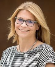 Eine Frau mit blonden Haaren, Brille und gestreiftem Oberteil.