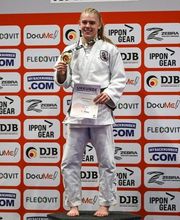 Eine junge Athletin präsentiert eine Medaille und eine Urkunde auf einer Siegerfläche. Das Bild transportiert Stolz und sportlichen Erfolg.
