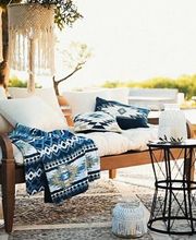 Eine stilvoll eingerichtete Terrasse mit Holzmöbeln, Textilien in Blau-Weiß und mediterranen Details lädt zum Entspannen ein. Das warme Sonnenlicht und die natürliche Umgebung erzeugen ein Gefühl von Urlaub und Leichtigkeit.