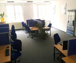 hier sind 9 Arbeitsplätze im Großraumbüro abgebildet mit je zwei Bildschirmen, Headset, Tastatur und Maus