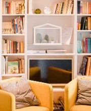 Gemütliche Sitzecke mit 2 gelben Sessel vor einem weißen Bücherregal mit einem kleinen Fernseher.