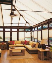 Ein stilvoller Wohnraum mit einer großen Glasfassade, die mit lichtdurchlässigen Plissees ausgestattet ist. Die Raumgestaltung schafft eine warme und einladende Atmosphäre.