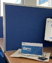 Arbeitsplatz bestehend aus 2 PC-Bildschirmen, Tastatur, Maus sowie einem blauen Bürostuhl und blauen Trennwänden.