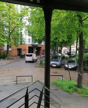 Eingangsbereich mit Blick auf den Parkplatz und die Straße. Es sind einige, grüne Bäume im Bild.