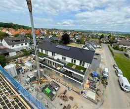 Blick über die Dachlatten auf die Baustelle eines Mehrfamilienhauses mit Turmkran. Neubau von AS-Bau.