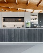 Diese moderne LEICHT Designküche verbindet klare Linien, hochwertige Materialien und intelligente Funktionalität zu einem stilvollen Gesamtkonzept. Die großzügige Kücheninsel mit grauer Holzstruktur bildet den Mittelpunkt der offenen Wohnküche und bietet viel Arbeits- und Stauraum. Helle Hochschränke, integrierte Elektrogeräte sowie offene Regale mit indirekter LED-Beleuchtung schaffen eine elegante und wohnliche Atmosphäre. Die Ausstellungsküche im Küchentreff Liebold zeigt zeitloses Küchendesign für höchste Ansprüche an Ästhetik und Komfort.