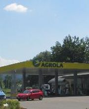 AGROLA Tankstelle in Buchrain mit TopShop; links grosses Totem-Schild mit Landi Logo, AGROLA Diskus Logo, digitaler Preisanzeige, AdBlue, TopShop und selfwash logo, vor Tankstelle rotes Auto