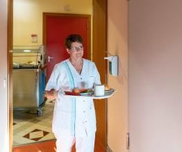 Verpflegungsassistentin bringt nicht gehfähigen Patienten das Essen auf das Krankenzimmer