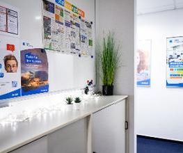 Flur mit einer Informationstafel und einem Sideboard darunter mit mehreren Pflanzen und einer Lichterkette..