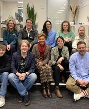 Gruppenbild vom Standortteam. 10 Personen sitzen im Flur auf einer Treppe und lächeln freundlich in die Kamera.