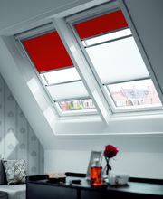 Ein modernes Dachfenster mit rotem Verdunkelungsrollo und halbtransparentem Plissee, das Lichtsteuerung und Privatsphäre ermöglicht.