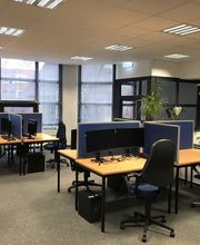 Schulungsraum mit mehreren Arbeitsplätzen mit jeweils 2 Bildschirmen, einem Bürostuhl, Tastatur, Maus und Headset. Mehrere Pflanzen stehen im Raum.