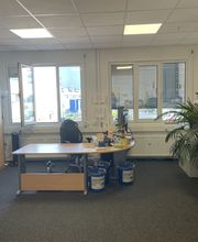 Ein Beratungsbüro mit einem Bogenschreibtisch, Büroschränken und einigen Zimmerpflanzen sowie einer Fensterfront.