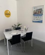 Ein weißer Tisch mit 4 schwarzen Stühlen auf dem ein Klemmbrett liegt sowie eine Blumenvase steht.