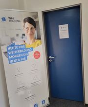 WBS TRAINING Werbeaufsteller mit der Aufschrift „Heute eine Weiterbildung. Morgen ein neuer Job.“ vor einer blauen Tür..