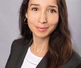 Junge Frau mit längen dunklen Haaren und schwarzem Blazer.