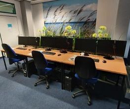 Schulungsraum mit mehreren PC-Arbeitsplätzen mit Monitor, Tastatur, Maus und Headset.