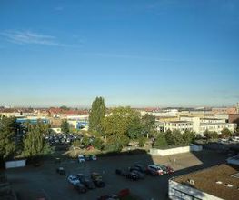 Ausblick vom Standort Braunschweig auf einen Parkplatz, mehreren Bäumen und Wohnhäuser