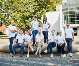 Team Region Bautzen-Görlitz, bestehend aus 9 Personen. Alle im weißen WBS GRUPPE T-Shirt am Brunnen vor einem Gebäude mit vielen großen Fenstern.