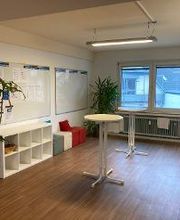 Aufenthaltsraum mit Zimmerpflanzen und Küche mit Sitzmöglichkeiten und Stehtischen.