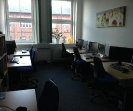 Schulungsraum mit mehreren Arbeitsplätzen mit jeweils 2 Bildschirmen, einem Bürostuhl, Tastatur, Maus und Headset.