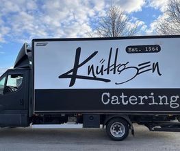 Professionell beschrifteter Catering-Lkw mit großflächigem Firmenlogo und kontrastreichem Design. Die klare Fahrzeugwerbung sorgt für hohe Sichtbarkeit und einen einheitlichen Markenauftritt unterwegs.