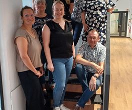 Ein Gruppenbild vom Team für den Kooperationsstandort Grimma. Die Personen stehen auf einer Treppe und lachen freundlich in die Kamera.