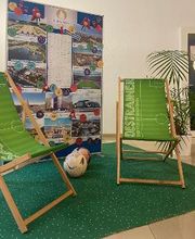 Foyer mit Fußballdekoration. 2 Liegestühle auf einem grünen Teppich und 2 Fußbälle. Dahinter ein Aufsteller mit verschiedenen Fotos und eine Zimmerpflanze. 