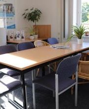 Ein Pausenbereich mit einem großen Tisch mit einer Pflanze und 8 verschiedenen Stühlen. Dahinter ein Tisch mit Flyern und Pflanzen, darüber ein Plakat der WBS TRAINING.