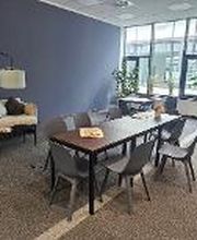 Gemütlicher Aufenthaltsraum mit Tischen und Stühlen, sowie einem modernen Sofa, einem Sitzkissen, einer stilvollen Stehlampe und mehreren Zimmerpflanzen.