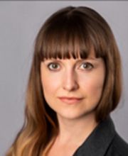 Portrait einer Mitarbeiterin mit langen, hellbraunen Haaren und Pony, die freundlich in die Kamera schaut.