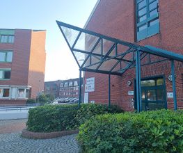 Außenansicht vom Gebäude. Backsteingebäude mit einer dunkelgrünen Eingangstür und Überdachung.