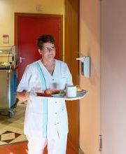 Verpflegungsassistentin bringt nicht gehfähigen Patienten das Essen auf das Krankenzimmer