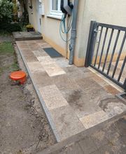 Neu gestalteter Hauszugang mit großformatigen Travertin Natursteinplatten und klarer Randeinfassung aus Granit. KK GaLaBau bei Berlin verbindet mit dieser Pflasterung den Hauseingang, das Gartentor und die seitlichen Außenflächen.