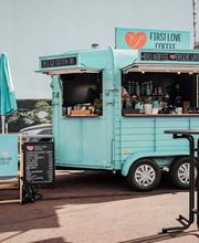 FirstLoveCoffee GmbH - Kaffee Catering Berlin - Türkiser Kaffeeanhänger mit Bio-Kaffee, Tee, frischen Waffeln, Stehtischen und Barista-Service bei einer Outdoor-Veranstaltung in der Stadt.