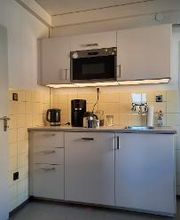 Küche mit mehreren Schränken, Wasserkocher, Kaffeemaschine und Kühlschrank.